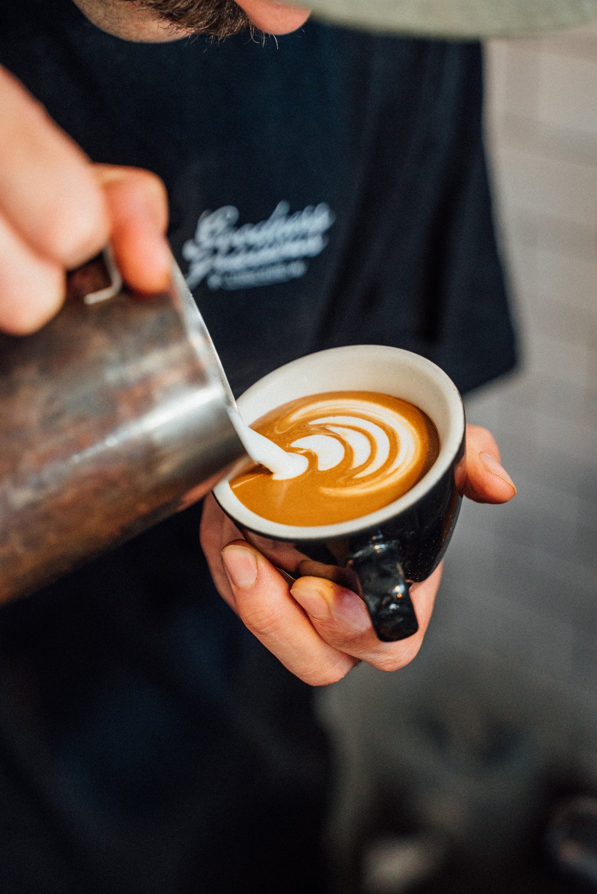 A barista's hands pouring milk into a flat white